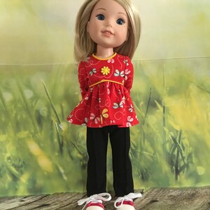 Op de afbeelding: Een pop met blond haar die een rood en geel bloempatroon top, een zwarte broek en rode sneakers draagt.
