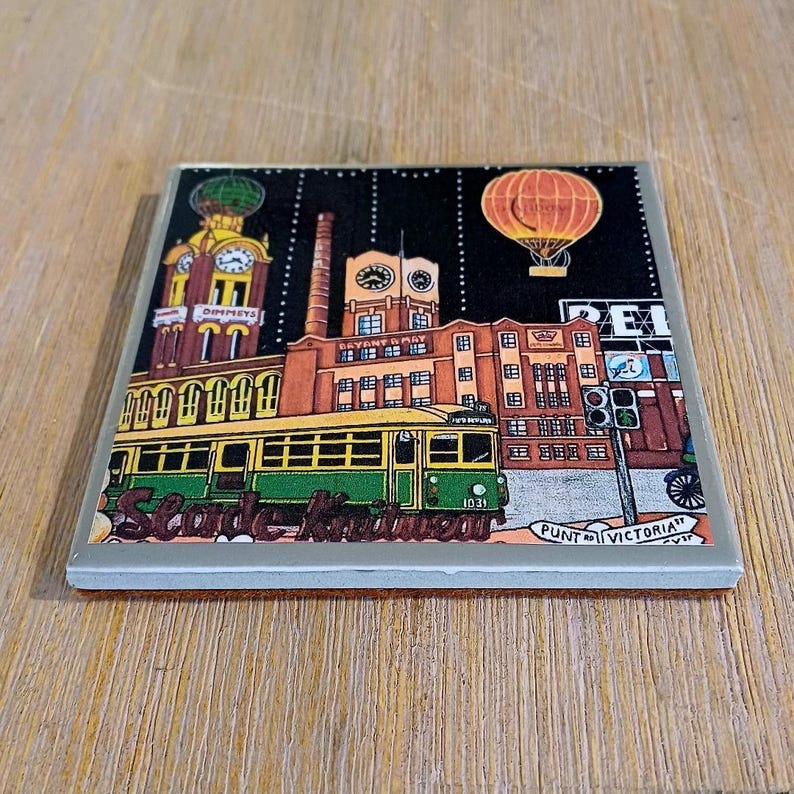 May include: A square coaster featuring a colourful illustration of a city scene with a green and yellow tram, a brick building labelled Bryant & May, a clock tower labelled Dimmeys, a hot air balloon, and text reading Slade Knitwear and Punt Rd Victoria.