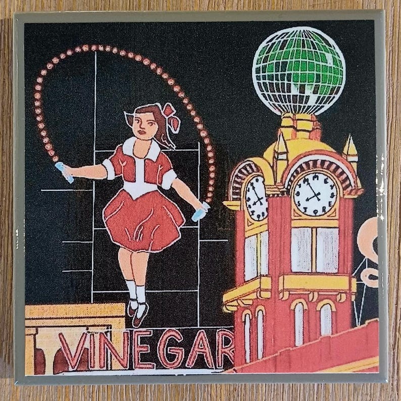 May include: A square decorative tile featuring a graphic illustration of a person jumping rope in a red dress. Beside them is a red clock tower topped with a green globe. The word VINEGAR is printed in large red letters at the bottom of the scene.