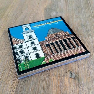Puede incluir: Un posavasos cuadrado con una colorida ilustraci&oacute;n de una torre blanca y un edificio cl&aacute;sico con columnas. Sobre los edificios, se representa un bote de remos con varios remeros contra un cielo azul brillante. Borde de color negro.