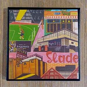May include: A square art print featuring a stylized urban landscape with a green sports field, a tiger graphic labeled Home of Richmond, a Nylex Plastics sign, and a building with the word Slade in large red script against a brick background.