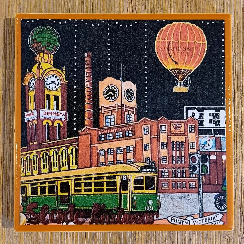 May include: A square decorative tile featuring a colourful illustration of a city street scene at night. A yellow and green tram travels past brick buildings, including the Dimmey's clock tower and Bryant & May factory, with a hot air balloon above.