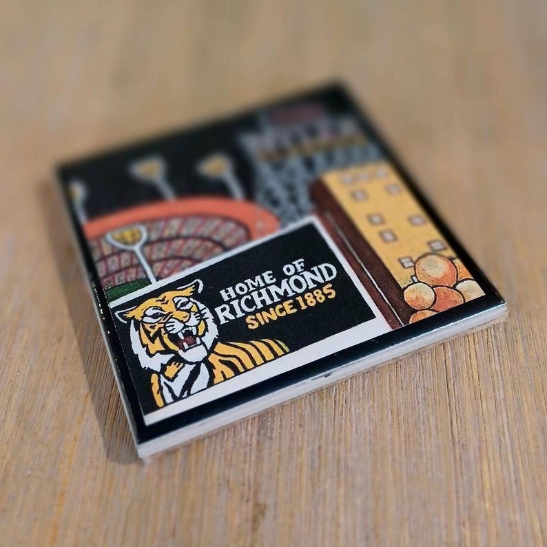 May include: A square ceramic coaster featuring a graphic illustration of a tiger head and the text HOME OF RICHMOND SINCE 1885. The design includes a stadium scene with orange seating and a yellow building structure on a black background.