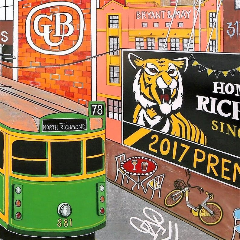 May include: A colorful painting depicting a green and yellow tram labeled North Richmond 78, passing a brick building with a GB logo, a Bryant & May sign, and a large billboard featuring a tiger illustration, the text 2017 PREM, a bicycle, and a cafe table.