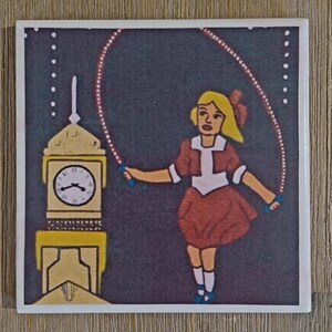 May include: A square ceramic tile featuring a graphic illustration of a person with blonde hair wearing a brown dress and white socks, jumping rope. Beside the person is a yellow clock tower with a white clock face against a dark background.