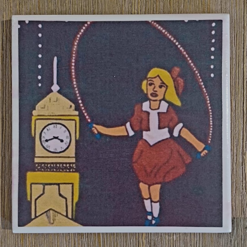 May include: A square ceramic tile featuring a graphic illustration of a person with blonde hair wearing a brown dress and white socks, jumping rope. Beside the person is a yellow clock tower with a white clock face against a dark background.