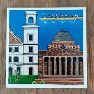 Puede incluir: Un azulejo cuadrado de cer&aacute;mica con una colorida ilustraci&oacute;n de una torre blanca y un edificio cl&aacute;sico con columnas. Sobre las estructuras, un bote de remos amarillo con ocho remeros aparece contra un cielo azul brillante. Incluye follaje verde.