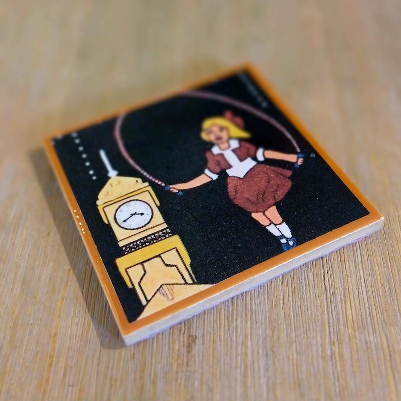 May include: A square ceramic tile featuring a black background with a graphic illustration of a blonde person in a brown dress jumping rope. Next to the person is a yellow clock tower with a white clock face and black hands. The tile has a light orange border.
