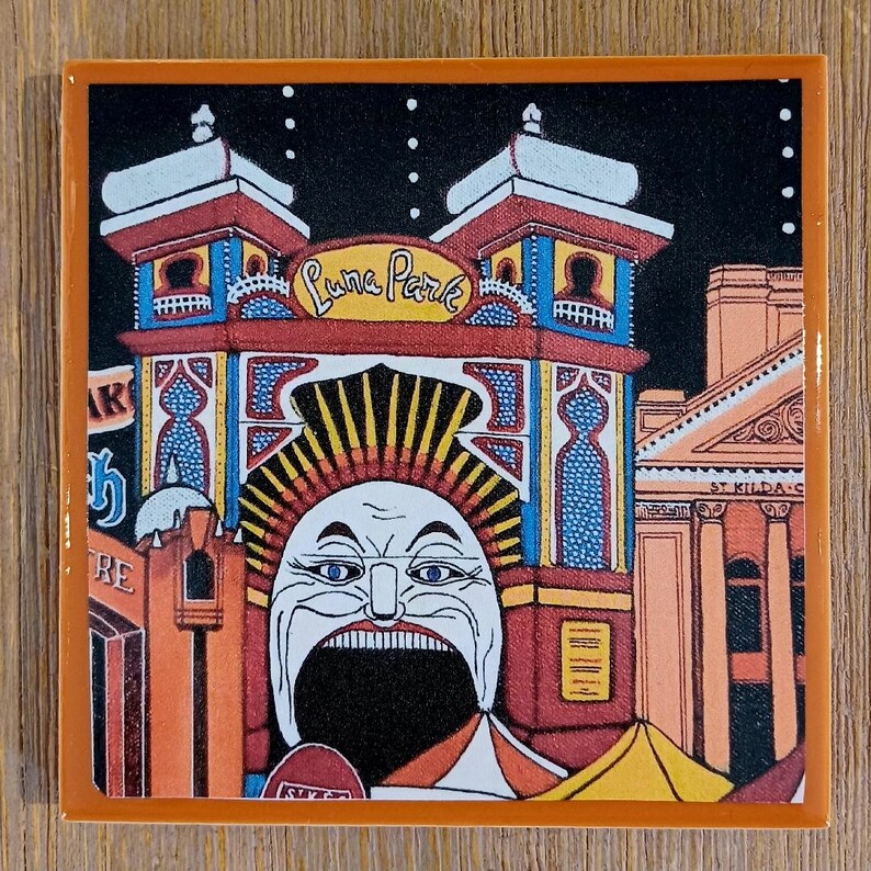 May include: A square ceramic tile featuring a colorful illustration of the Luna Park entrance in St. Kilda. The design displays the iconic face with a wide open mouth, red and blue architectural towers, and the text Luna Park against a black sky.