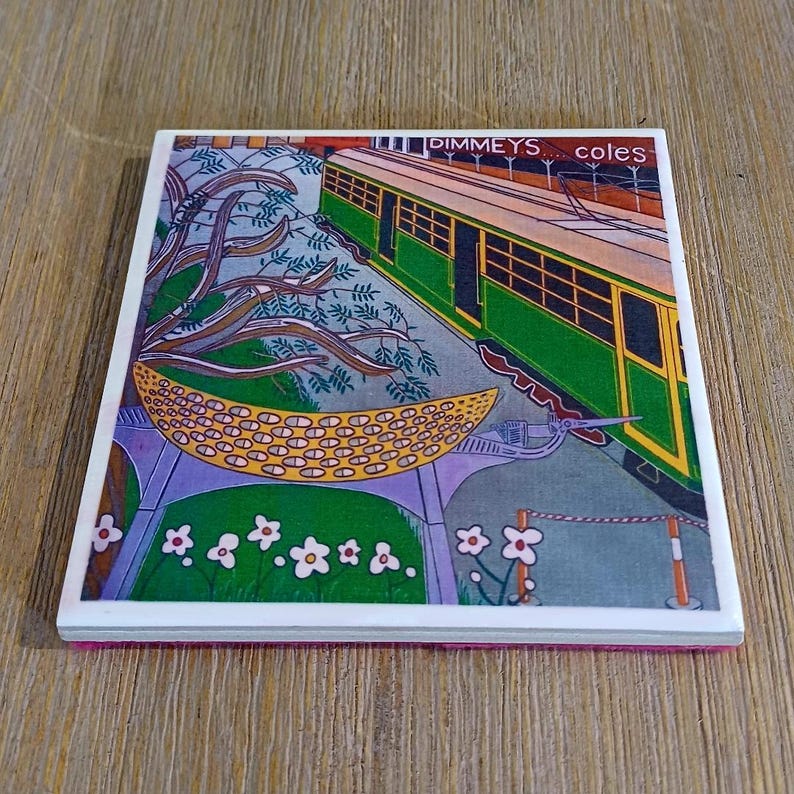 K&ouml;nnte beinhalten: Ein quadratischer Keramikuntersetzer mit einer farbenfrohen Illustration einer gr&uuml;nen und gelben Stra&szlig;enbahn. Der Text DIMMEYS... coles ist oben aufgedruckt. Die Szene zeigt stilisiertes violettes Blattwerk, eine gelbe gemusterte Mondsichel und wei&szlig;e Blumen.