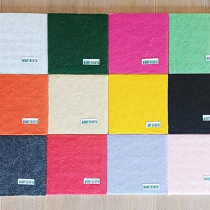 May include: A collection of twelve square felt sheets arranged in a grid, featuring a variety of colors including white, dark green, hot pink, light green, orange, cream, yellow, black, dark gray, red, light blue, and light pink.