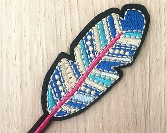 Puede incluir: Un parche bordado de pluma azul, blanco y rosa con borde negro. El parche mide 7,5 x 2,5 cm.