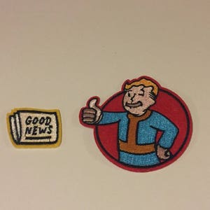 Pode incluir: Dois patches bordados, um com um personagem de desenho animado dando um polegar para cima e o outro com as palavras "Good News" em um fundo amarelo.