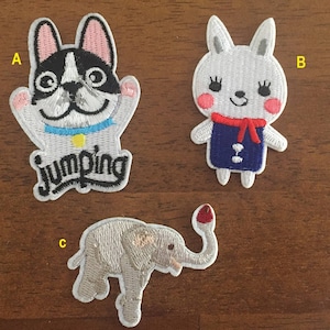 May include: Three embroidered iron-on patches featuring a white dog with black spots, a white rabbit with red and blue accents, and a grey elephant with a red trunk. The dog patch has the word "Jumping" embroidered on it.