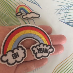 以下が含まれることがあります： 雲と「Oh」と「Yeah!」の刺繍が施された虹のアイロン接着パッチ2枚