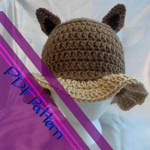 May include: A crocheted hat with brown and beige yarn, featuring two floppy ears on top. The hat is displayed on a white mannequin head. The text "PDF Pattern" is visible in the image.