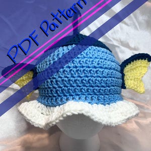 May include: A crocheted blue and white fish hat with yellow fins. The hat has a ruffled brim and a blue and white striped pattern.