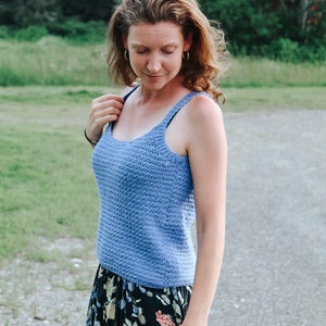 May include: A woman wearing a light blue crocheted tank top and a black floral skirt.
