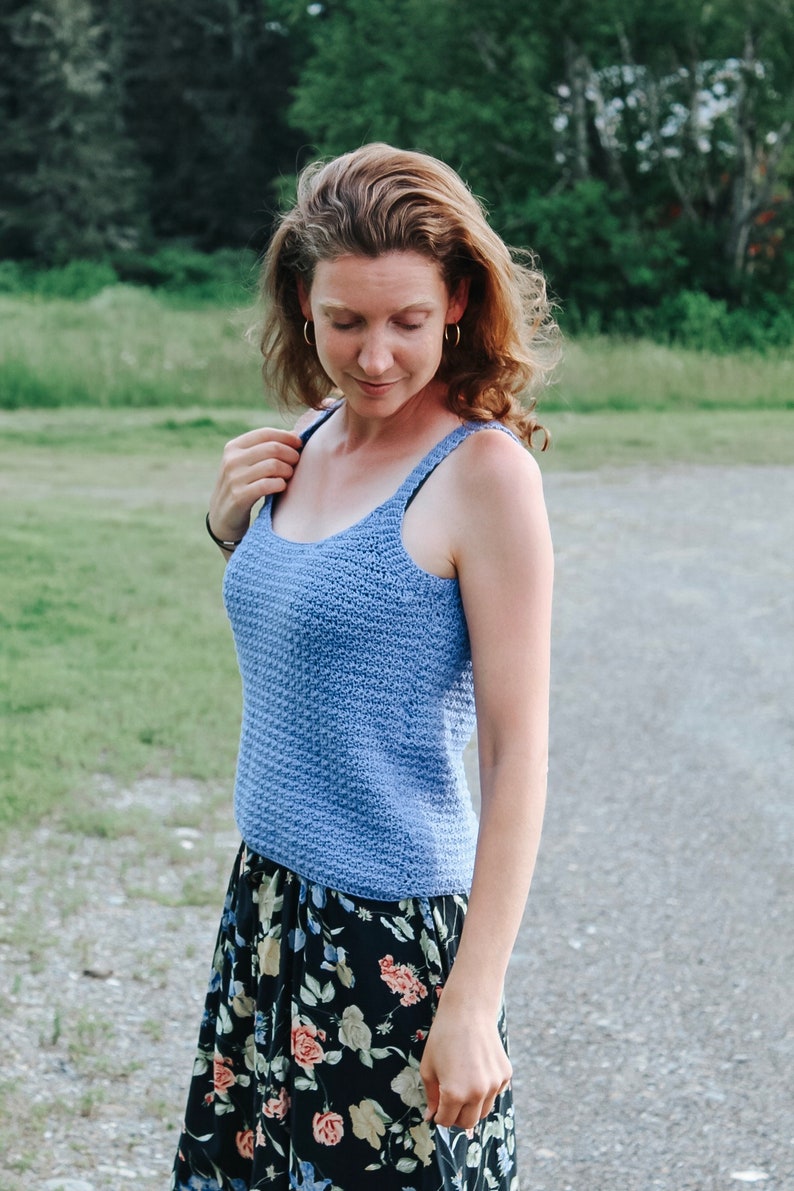 May include: A woman wearing a light blue crocheted tank top and a black floral skirt.
