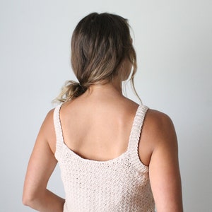 May include: A beige crochet tank top with thin straps. The top is made with a textured stitch and has a scoop neck.