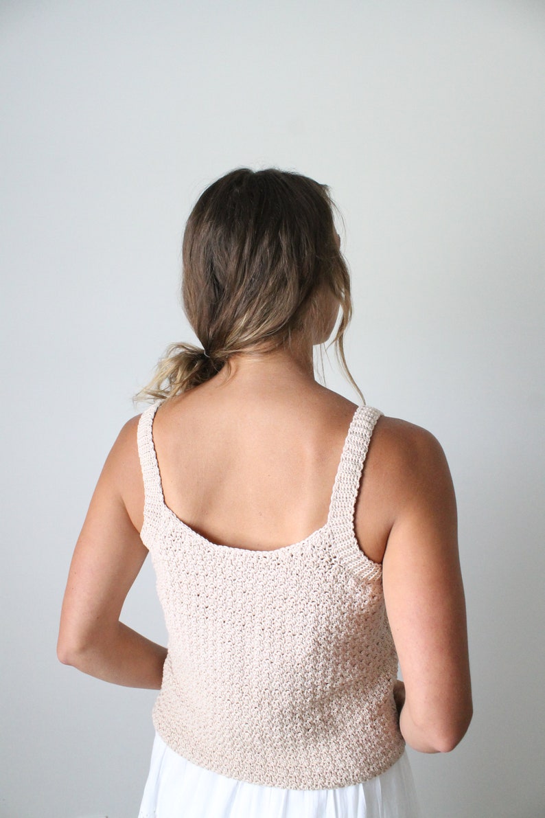 May include: A beige crochet tank top with thin straps. The top is made with a textured stitch and has a scoop neck.