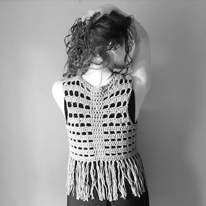 May include: A crocheted vest with a fringe trim. The vest is made with a light brown yarn and has a delicate openwork pattern.