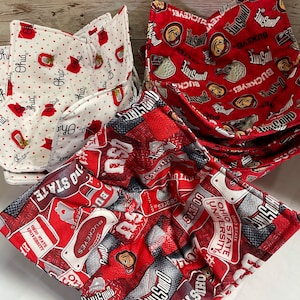 May include: Three fabric bowl cozies featuring Ohio State University branding. One cozy is white with red polka dots and Ohio logos, while two are red with repeating Ohio State, Buckeyes, and mascot graphics in white, black, and gray.