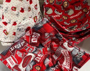 May include: Three fabric bowl cozies featuring Ohio State University themes. One cozy is white with red dots and Ohio logos. Two cozies are red with various Ohio State Buckeyes graphics, including helmets, text, and mascot faces, with quilted stitching.