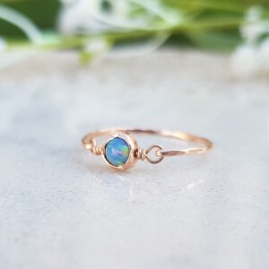 May include: A delicate gold ring with a small, iridescent opal gemstone. The ring is made of thin wire and has a simple, elegant design.