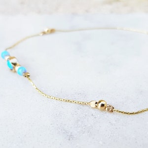Könnte beinhalten: Ein zartes Armband aus goldener Kette mit kleinen blauen und weißen Perlen und einem goldenen Perlenakzent.