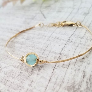 Peut inclure: Un bracelet délicat en or avec une pierre précieuse bleu clair. Le bracelet est fait de fil fin martelé et a un fermoir simple.