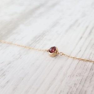 Peut inclure: Un collier délicat en chaîne dorée avec un pendentif en pierre rouge.