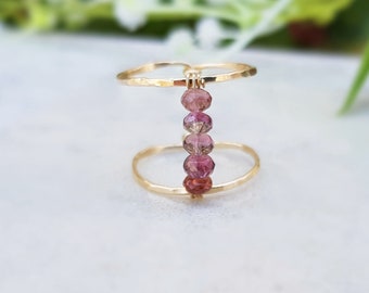 May include: A gold ring with two bands and a row of pink and red gemstones.