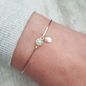 Könnte beinhalten: Ein zartes goldenes Armkettchen mit einem kleinen Opal-Anhänger und einem herzförmigen Anhänger.