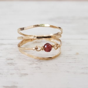 Puede incluir: Un anillo de oro con tres bandas y una pequeña piedra preciosa roja en el centro.