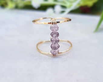 May include: A gold ring with a hammered finish and a row of five light purple beads.
