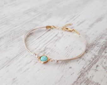 May include: A delicate bracelet with a light blue opal gemstone wrapped in gold wire. The bracelet is made with two strands of cream-colored cord.