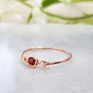 May include: A delicate rose gold ring with a small, round, red gemstone set in the center.