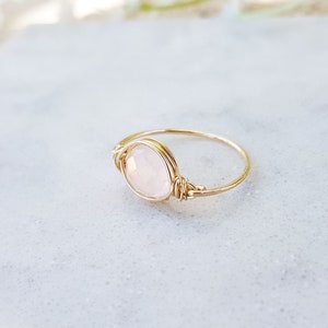 Puede incluir: Un delicado anillo de oro con una piedra preciosa rosa pálida engastada en un diseño de alambre envuelto.
