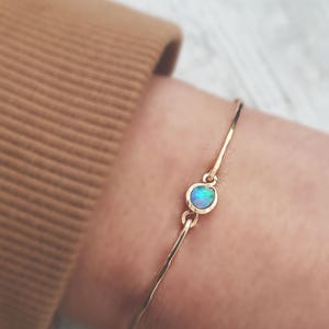 Peut inclure: Un bracelet fin en or avec un seul opale. L'opale est d'une couleur bleu-vert vibrante.