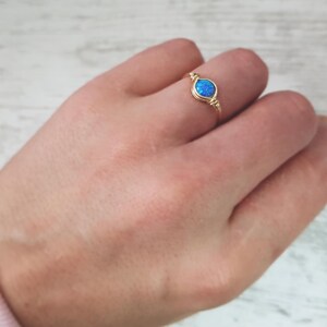 May include: A gold wire ring with a blue opal gemstone. The ring is on a person's finger.
