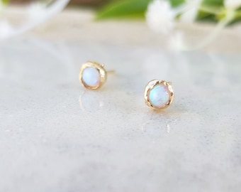 May include: A pair of gold earrings with small white opal stones set in a textured gold setting.