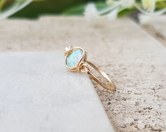 May include: A delicate gold ring with a wire-wrapped opal gemstone. The opal is a pale blue-green color with a subtle shimmer.