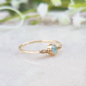 May include: A delicate gold ring with a light blue oval gemstone set in the centre. The ring band is thin and has a delicate leaf design.