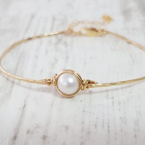 Puede incluir: Un delicado brazalete de oro con un solo acento de perla blanca. El brazalete es simple y elegante, perfecto para el uso diario.