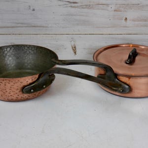 May include: A set of two copper pots with hammered surfaces. The smaller pot has a black handle and the larger pot has a lid.