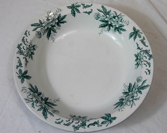 May include: A white ceramic bowl with a green floral design around the rim. The bowl is round and has a smooth, white interior.