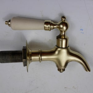 Peut inclure: Un robinet en laiton doré avec une poignée en céramique blanche. Le robinet a un bec qui s'incurve vers le bas et une base filetée.