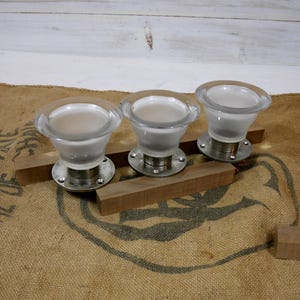 May include: Three clear glass and metal cabinet knobs with a frosted interior. The knobs are mounted on a silver base and sit on top of wooden planks. The knobs have a rounded, flared shape.