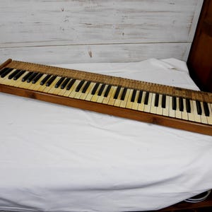 May include: A vintage piano keyboard assembly featuring a wooden frame, white and black keys, and an exposed internal mechanism with wooden components visible along the top edge of the keybed, presented as a standalone musical instrument part.